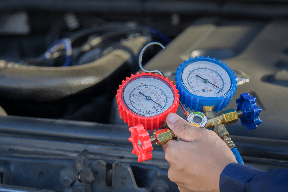 a/c repair. Auto repair shop in Republic, MO. Yocum Automotive. Image of a technician using a manifold gauge set to test the air conditioning system under the hood of a vehicle. Highlights precise A/C pressure readings for accurate repair.