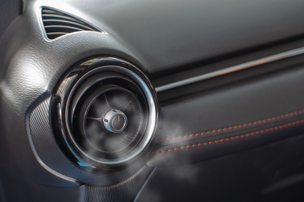 car a/c smells bad. Auto repair shop in Republic, MO. Yocum Automotive. Cold air visibly blowing out of a round car A/C vent on a black dashboard with red stitching detail.