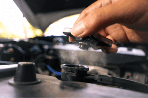 car overheat. Auto repair shop in Republic, MO. Yocum Automotive. Hand opening a steaming radiator cap on a vehicle’s cooling system. This image illustrates overheating issues and the importance of coolant system checks during hot weather.