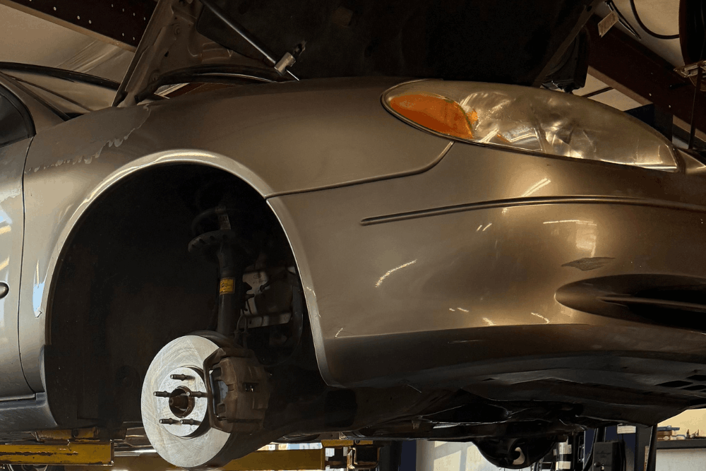 Brake problems, auto repair in Republic, MO by Yocum Automotive. Image of a vehicle on a lift with the front wheel removed, exposing the brake rotor and caliper. Highlighting reliable stopping power, thorough inspections, and safe everyday driving performance.