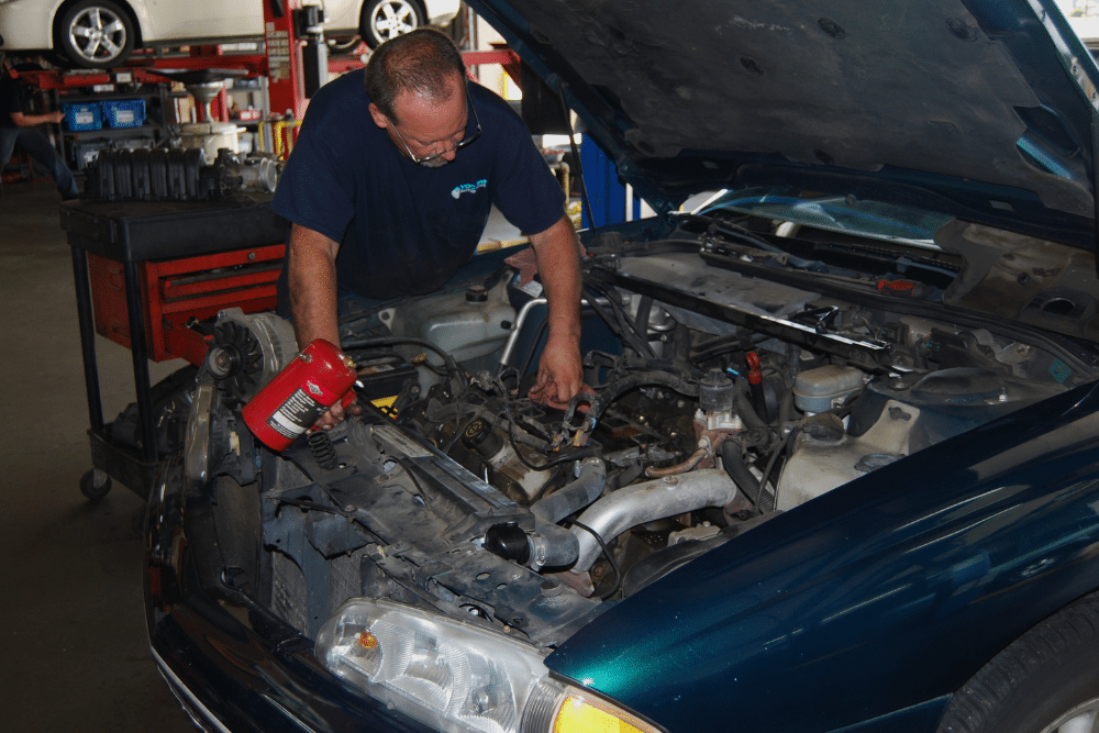 Engine Repair Service in Republic, MO At Yocum Automotive. Mechanic inspecting a car engine bay for summer maintenance in an auto repair shop.